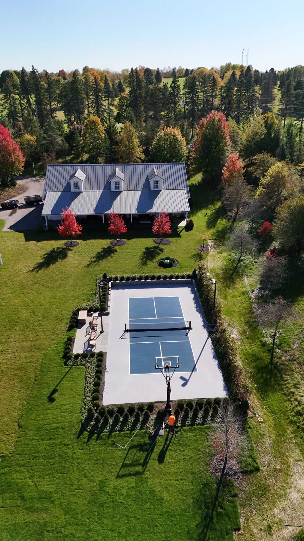 Aerial view of a private pickleball court behind a home, surrounded by hedges and fall color
