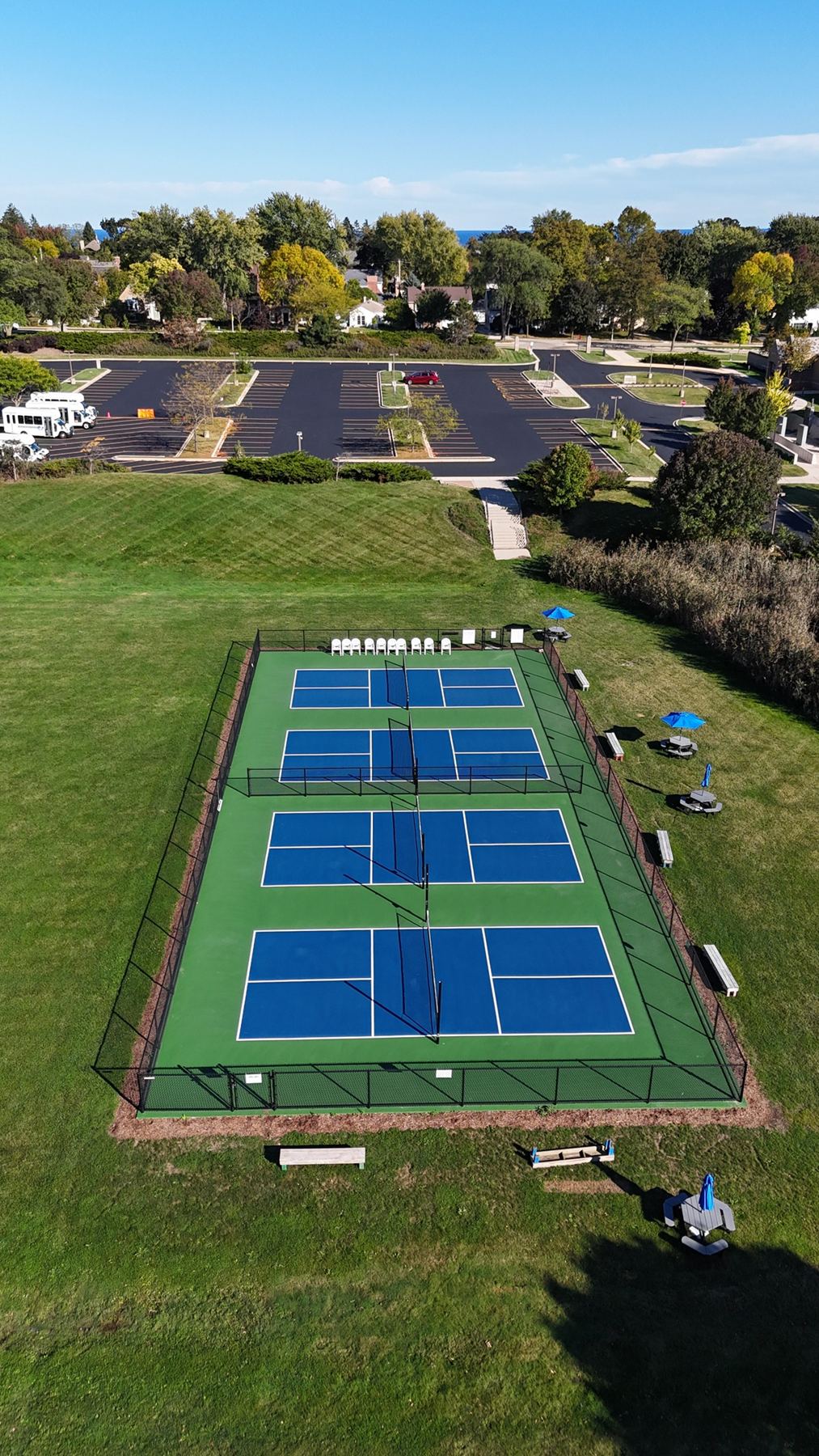 Aerial view down the length of four fenced courts with spectator chairs, benches and picnic tables